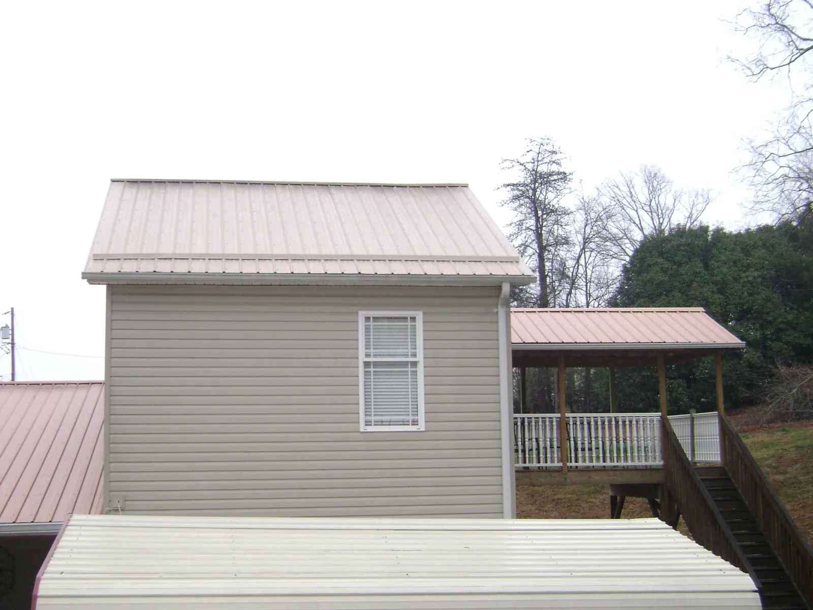 Tan metal roofs on a two story addition and attached porch, from a Roof Replacement job in Morton
